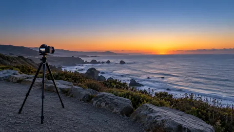 Editorial illustration of a tripod-mounted camera overlooking a coast before sunrise.